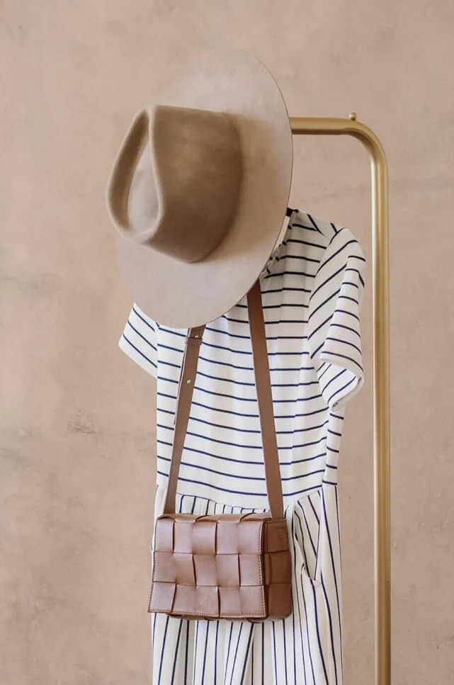 Hanger with stylish clothing hanging on it: purse, dress with stripes and a hat